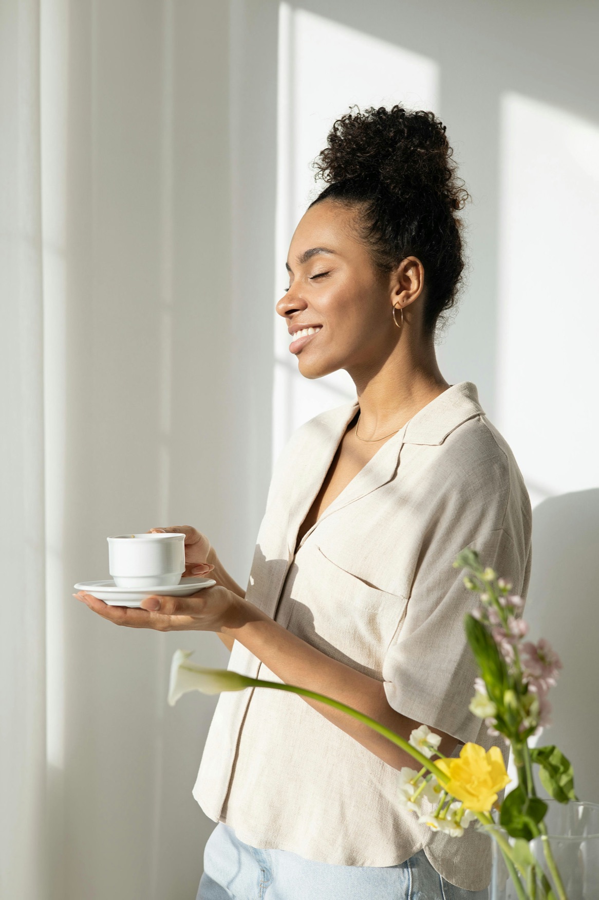 Woman smiling peacefully with her eyes closed, holding a cup of coffee in a sunlit room, representing individual relationship therapy in San Francisco, California